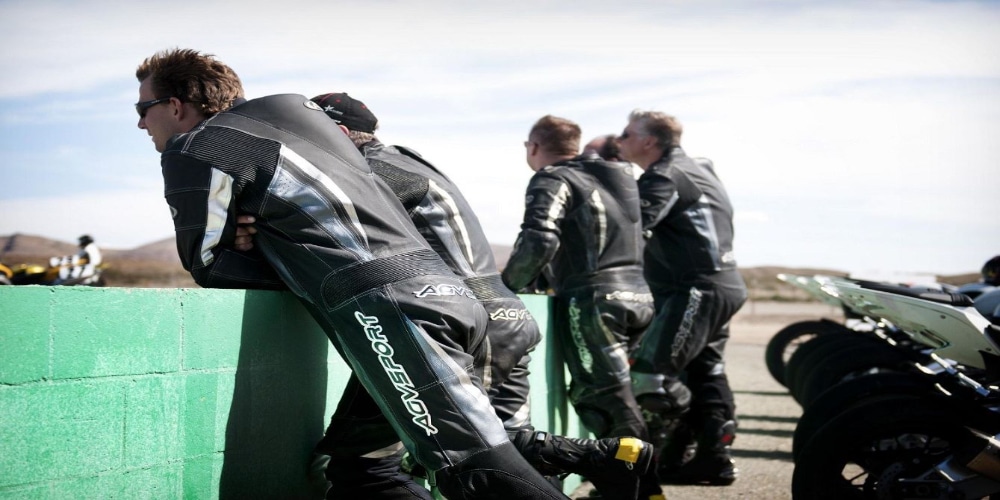 How Do You Break in a Motorcycle Race Suit? My 7 Dos And Don’ts Five instructors from the California Superbike School, dressed in AGVSPORT leather suits (including the AGVSPORT Monza Race Suit), watch their students ride while their bikes are parked in the background. Wearing the suit regularly can help break it in faster.