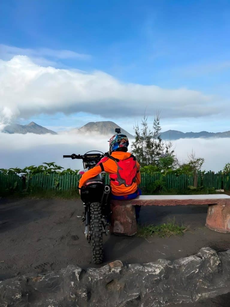 A rider, relishing the view on a less crowded day, finds solace next to an enduro bike, cradling it close, reminiscent of a trusted companion.