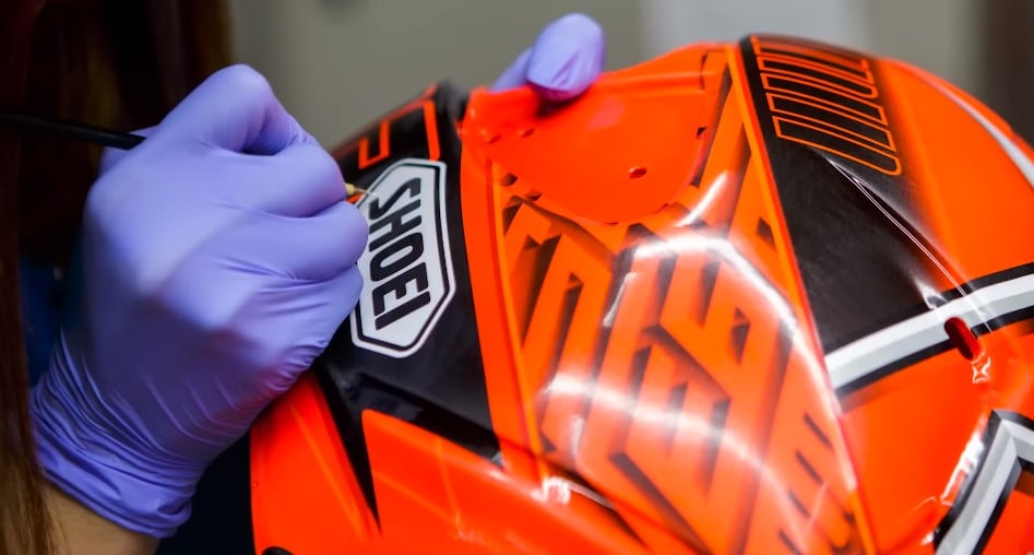 Refining the Shoei logo on the new Shoei Neotec 3, the most advanced flip-up sport, tour, and city helmet today. While the application of solid colors is mostly automated, the intricate graphics are painstakingly hand-applied. Any minute imperfections are meticulously corrected with brushwork before the final clear coat is applied to each and every helmet. Yeah, it's a meticulous and detailed process!