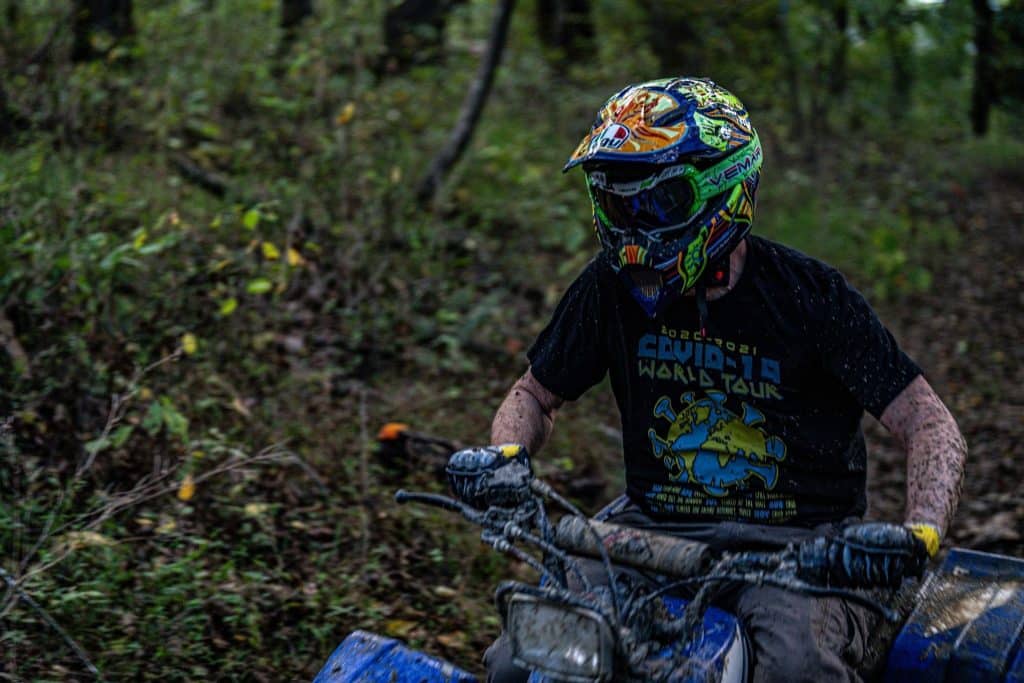 The AGV AX-8 dual sport helmet gets all mucky, indicating my intense ATV riding experience. I rely on this specialized helmet, featuring a chin bar for protection and compensating for restricted airflow with large vents. It offers versatile configurations, as seen with a peak and goggles, without a visor, allowing me to adjust airflow precisely for various riding conditions.