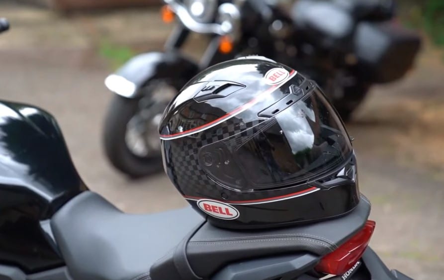 Top 7 Best Helmets for Naked Motorcycles Bell Qualifier DLX Mips helmet placed on a Honda motorcycle pavilion seat, featuring a closed visor integrated with Transition Adaptive technology. This innovative feature ensures the shield is transparent at night, darkens in sunlight, blocking harmful UV rays, and offers excellent anti-fog protection.