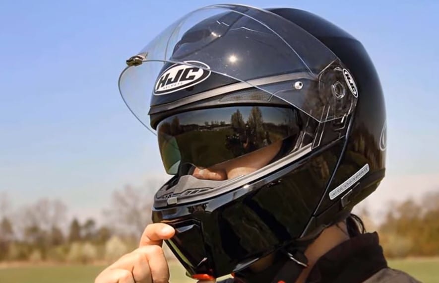 Right hand about to flip up the HJC RPHA 90S Carbon helmet. As a modular helmet, it allows you to effortlessly open and close the chinbar. Includes an internal sun visor for added convenience.