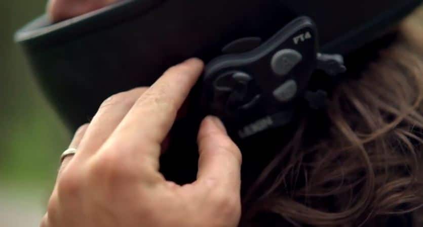 Rider adjusting the volume wheel on the side of their Bluetooth intercom system to increase the sound level while on a call or listening to audio, turning it clockwise to raise the volume.