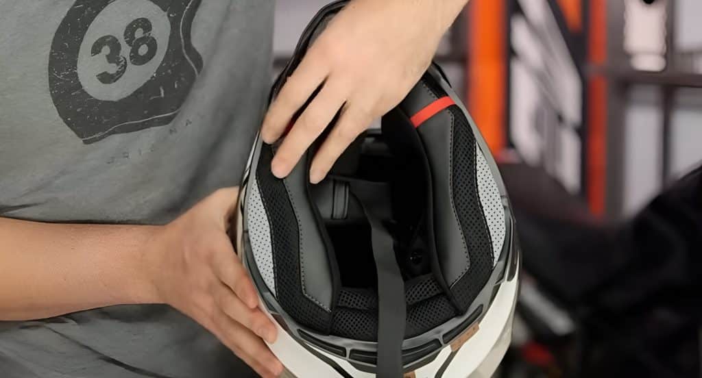 Checking the interior padding and chin strap of a motorcycle helmet to ensure it remains safe, clean, and properly fitted.