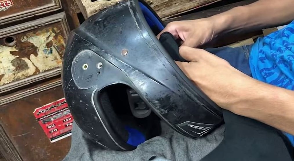 Technician examining a scratched black motorcycle helmet, checking the shell and padding for wear or damage before repair.