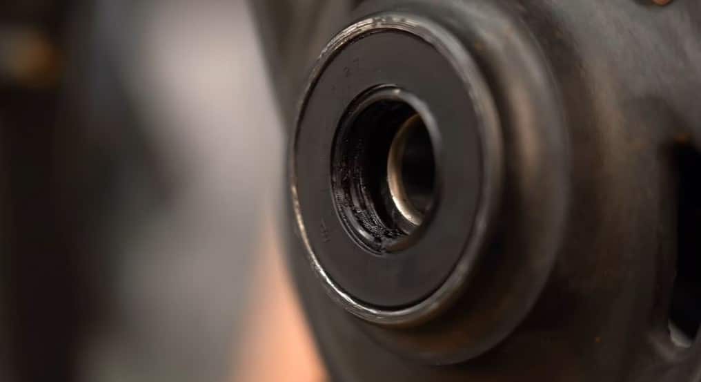 Close-up of a motorcycle wheel hub showing a worn and partially exposed wheel bearing with dark, contaminated grease around the seal.